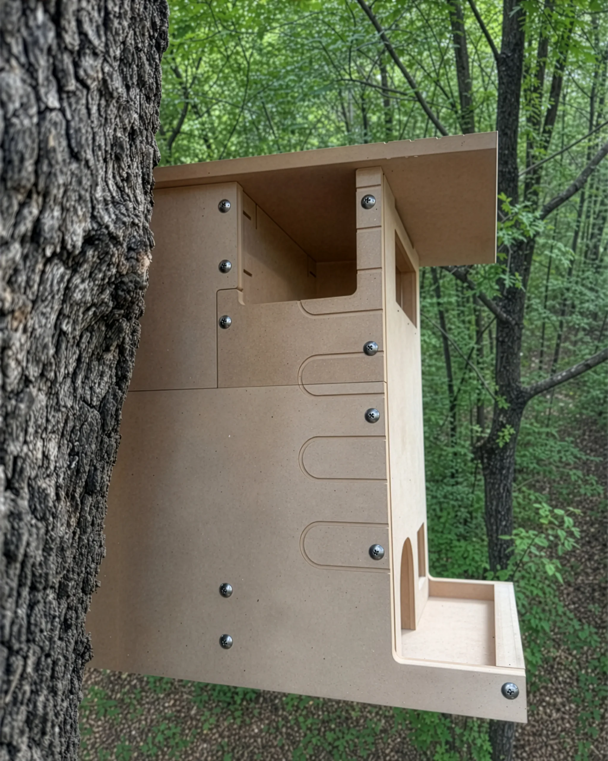 Wooden birdhouse mounted to a tree in a forest, with visible screws and an open front panel for nesting.